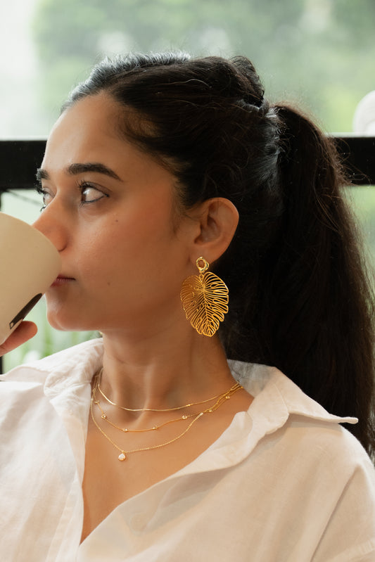 Woman wearing gold earrings and necklaces, holding a cup.