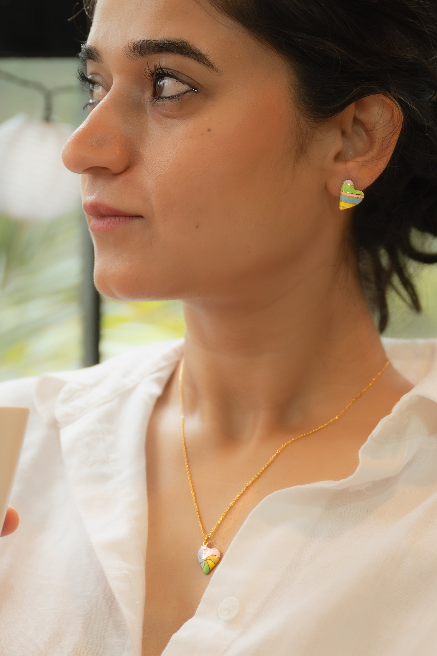 Close-up of a woman wearing a gold necklace and colorful earring with a blurred outdoor background