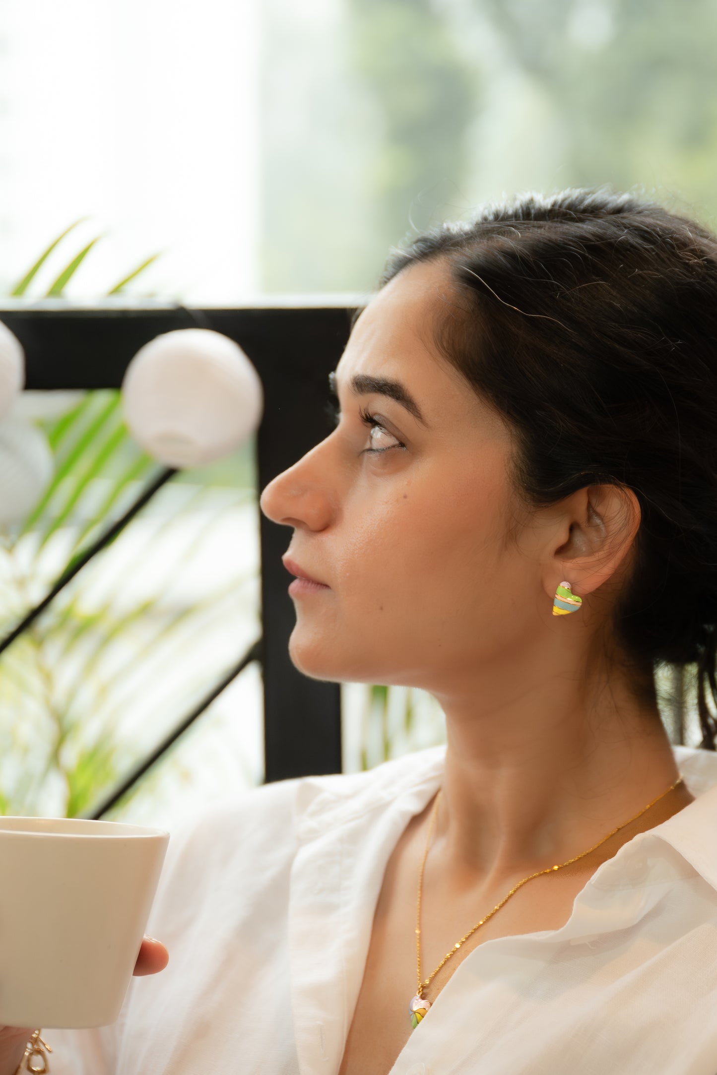 Woman holding a cup, looking out of a window with greenery outside