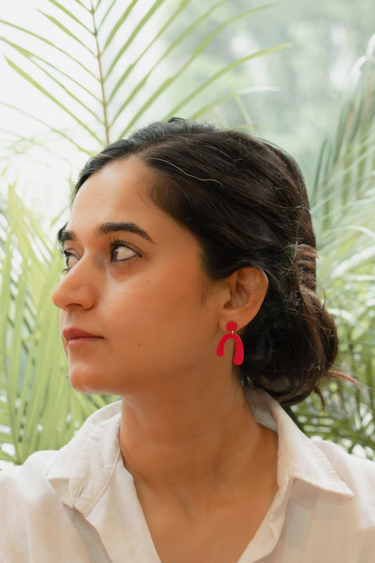 Woman wearing red earrings with a blurred green foliage background