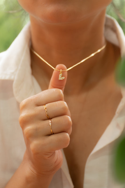 Person wearing a gold necklace and ring with a blurred green background