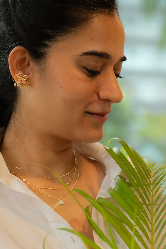 Woman wearing gold earrings and necklaces with a blurred green background