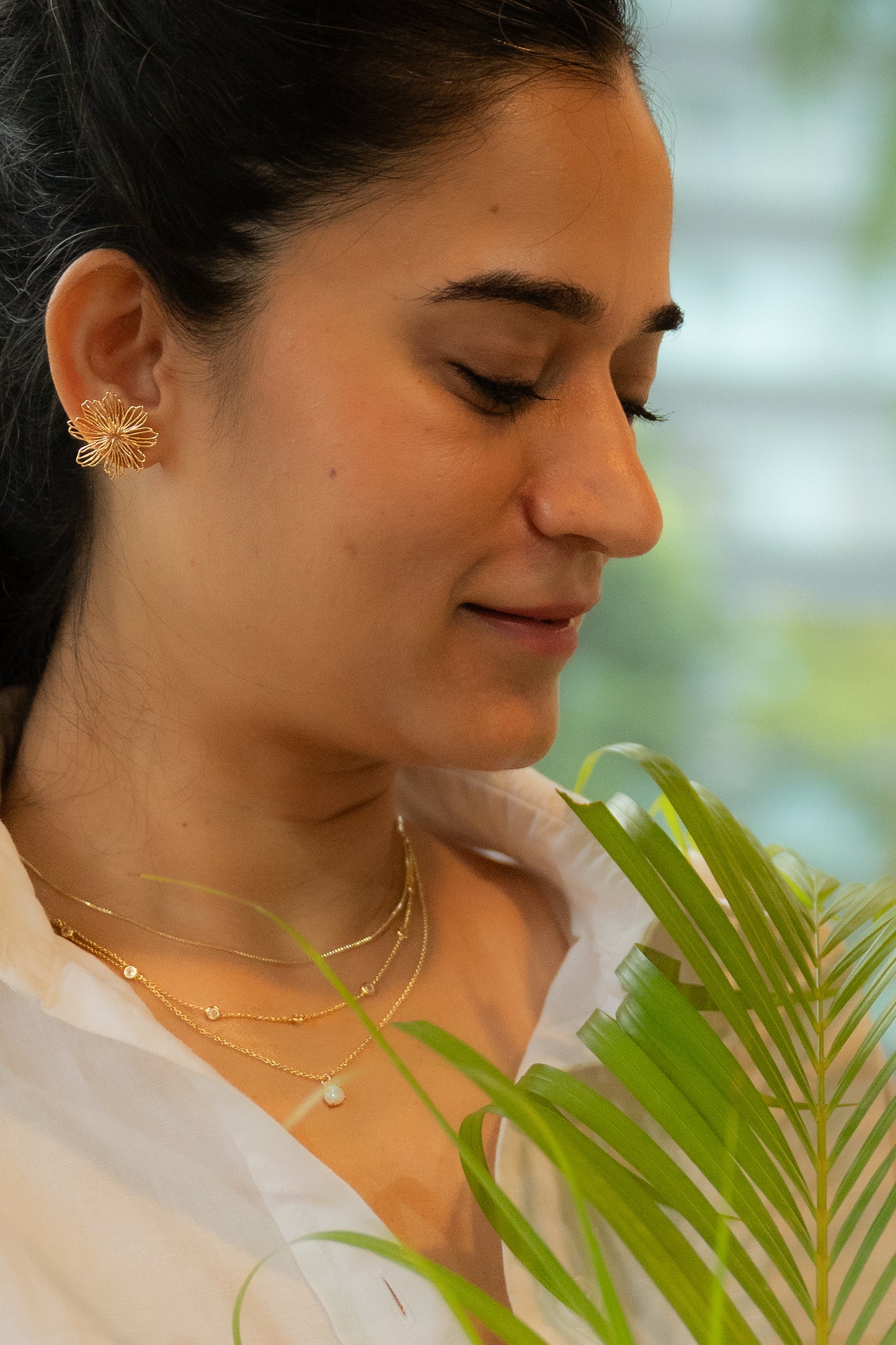 Woman wearing gold earrings and necklaces with a blurred green background