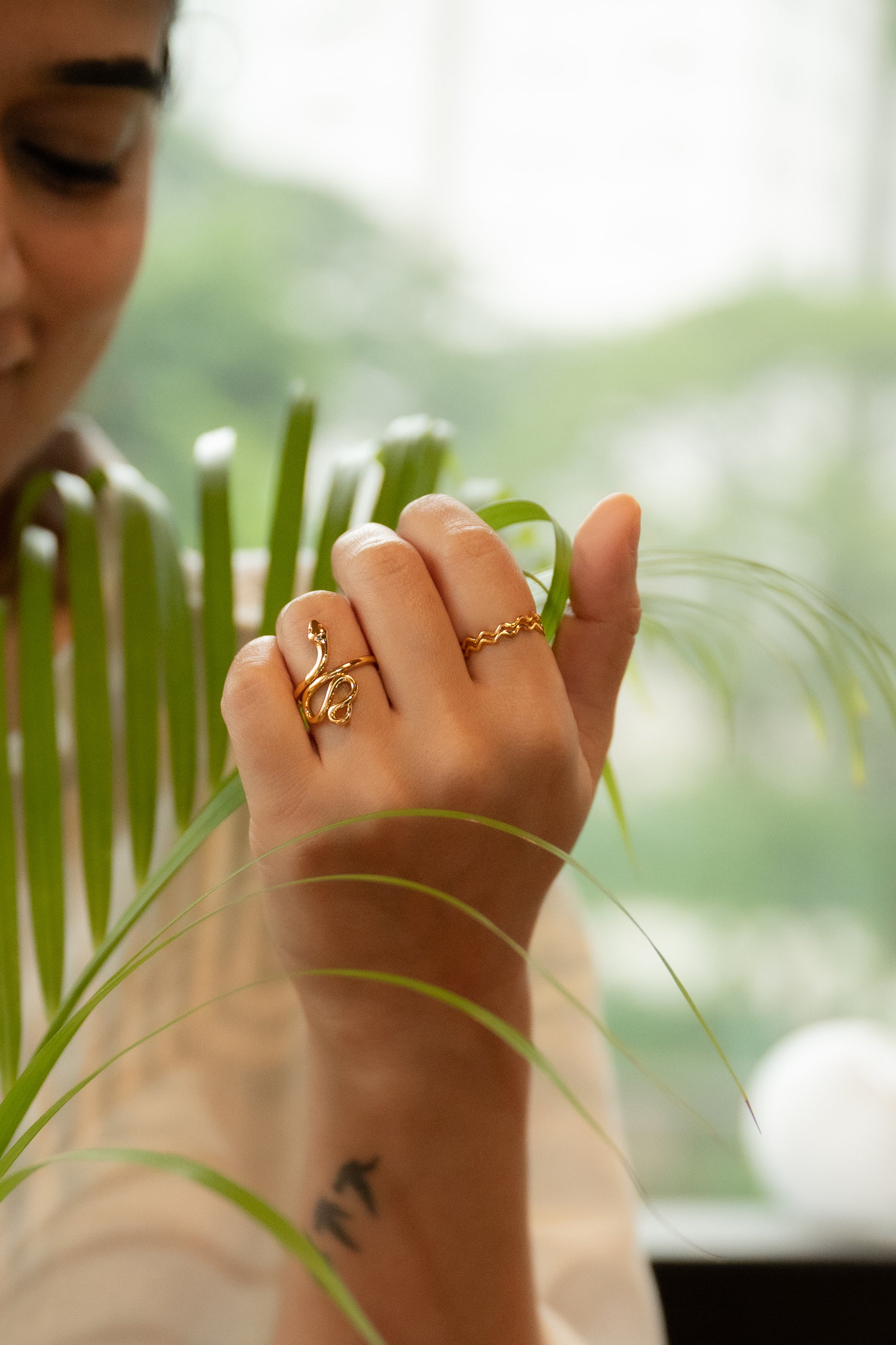 Person wearing a gold ring on a blurred green plant background