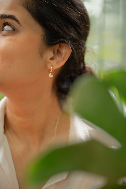Woman wearing gold earrings with green foliage in the foreground