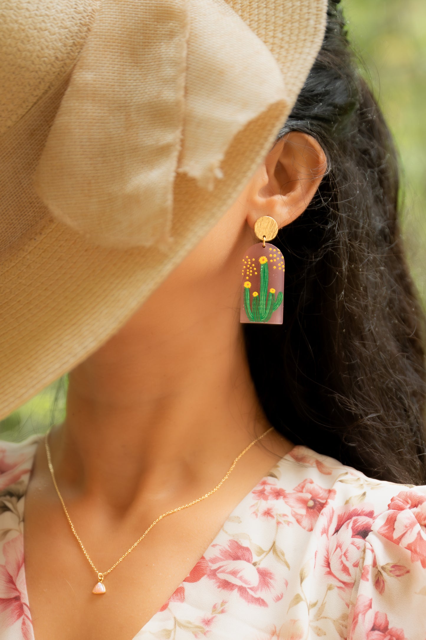 Person wearing a straw hat and colorful earrings with a blurred natural background