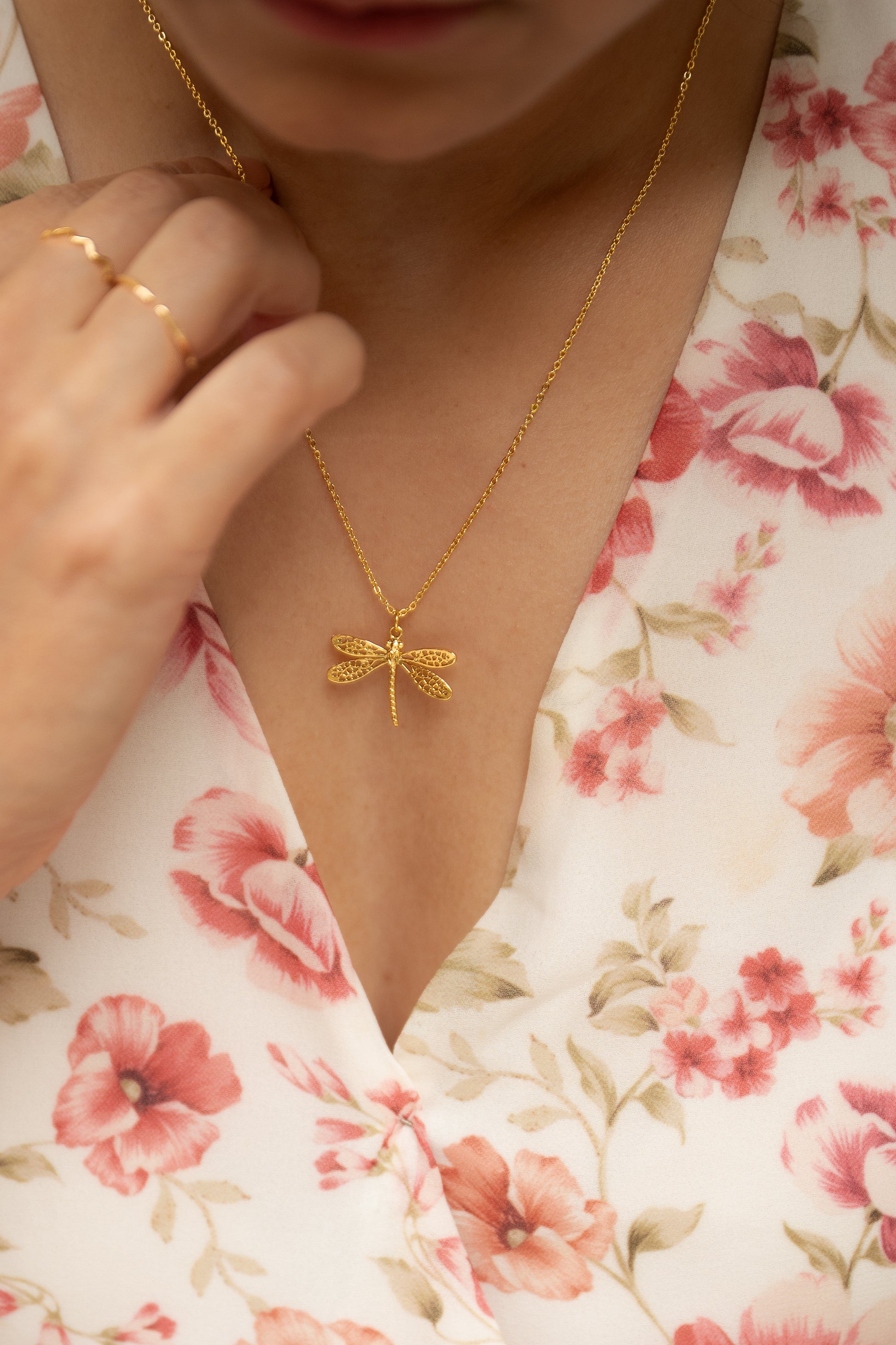 Gold necklace with a dragonfly pendant worn by a person in a floral outfit.