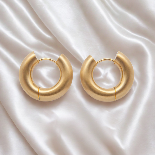 Gold hoop earrings on a satin surface