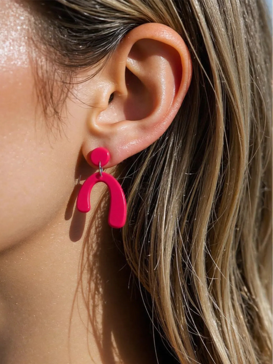 Close-up of a person wearing bright pink earrings with a neutral background